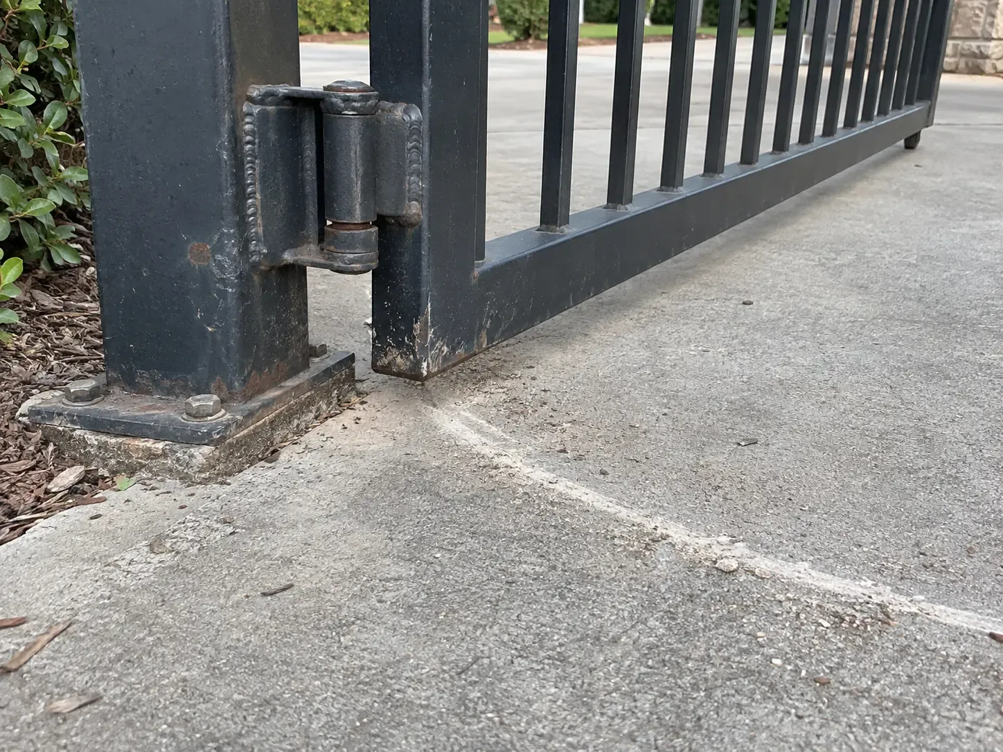 The hinge joint between a swing gate and its post, with the scrape arc the dragging gate has worn into the driveway below.